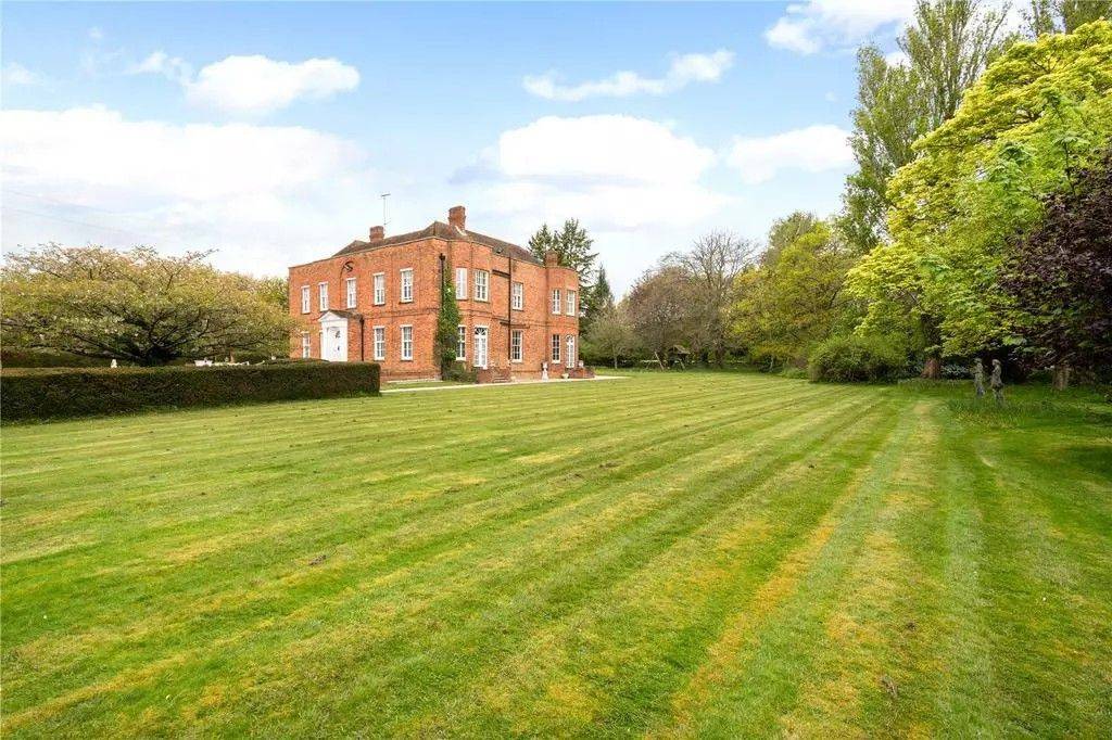 Wide view of the red-brick period country estate house surrounded by vast rolling lawns and mature trees in Reading RG10 by Love Locations.