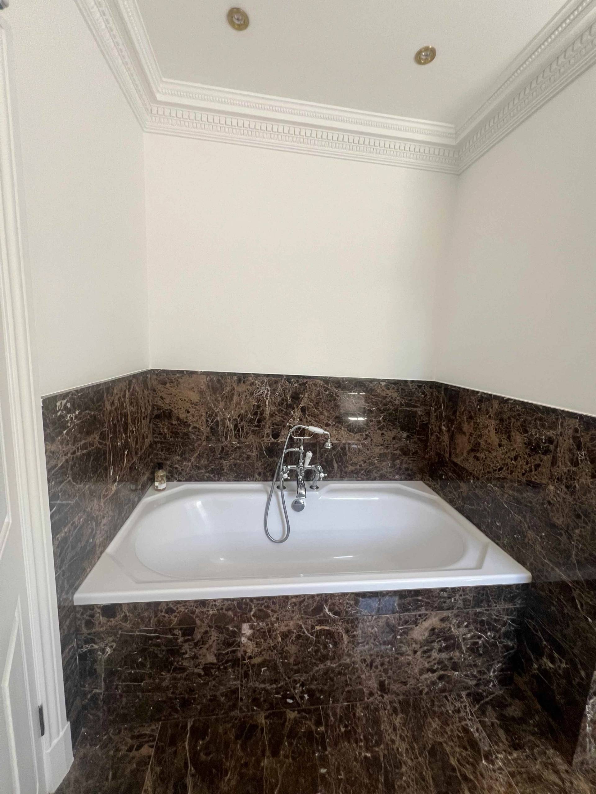 Inset bathtub surrounded by dark brown marble tiles and brass taps in a luxury bathroom, Love Locations BR7.