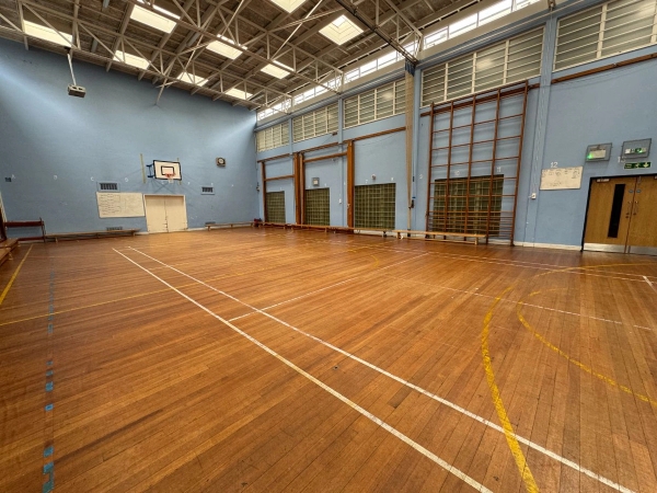 Love Locations school gymnasium shoot space EN4: High-ceilinged indoor sports hall with multi-sport lines on a classic timber floor, tailored for athletic training videos and feature film sports scenes.
