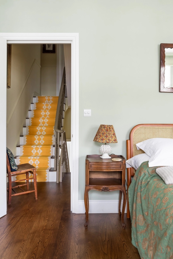 Charming London shoot location bedroom in Westminster SW1V from Love Locations, showcasing a mustard yellow runner on the staircase leading directly into a bedroom with a cane headboard.