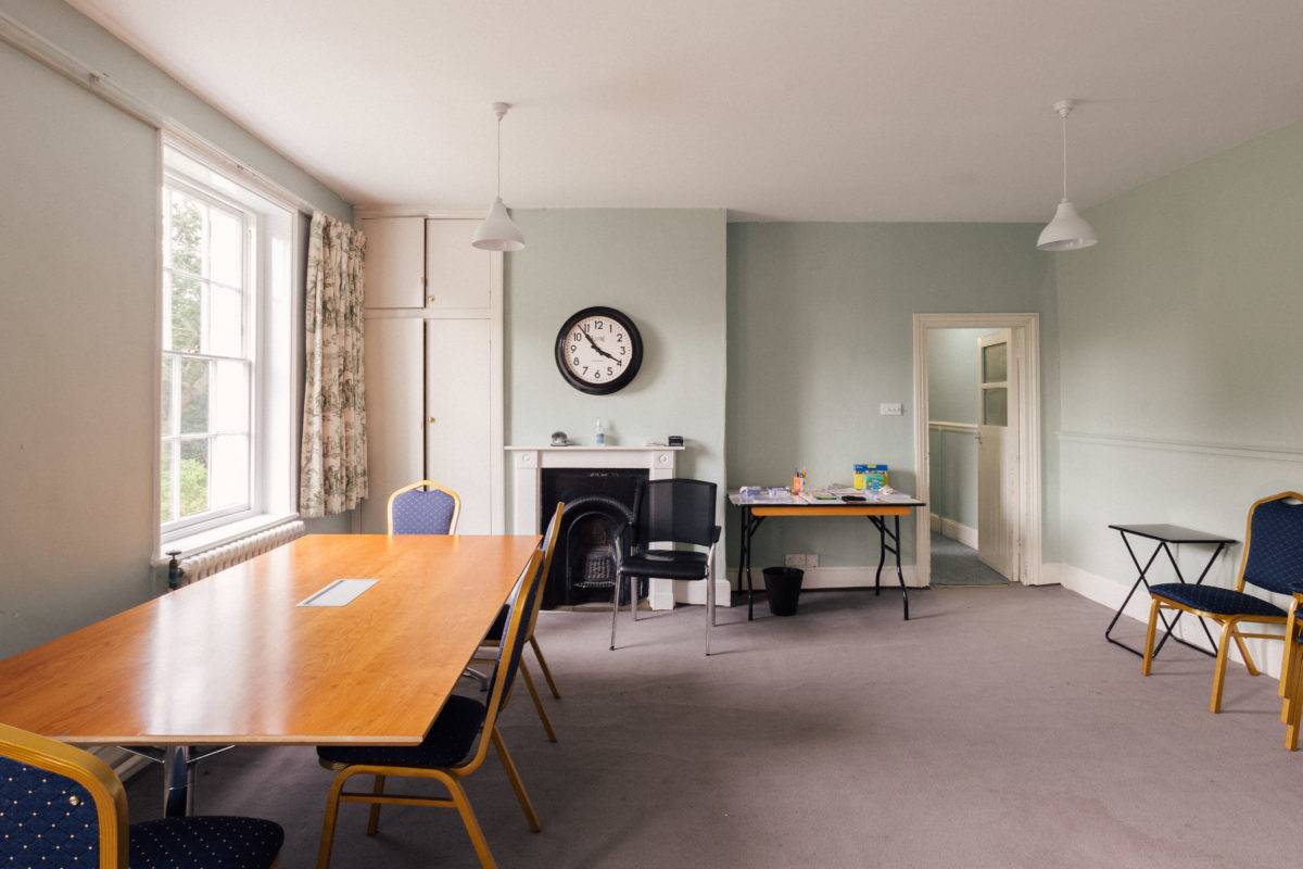 Large conference room or office space featuring soft green walls, wooden tables, and a period fireplace, Love Locations.