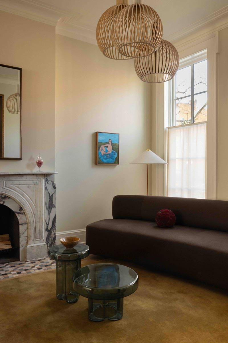 Elegant living room filming space in a 19th-century townhouse in Brooklyn NY 11217 by Love Locations, featuring neutral walls, a grey velvet sofa, a marble fireplace, and artwork.