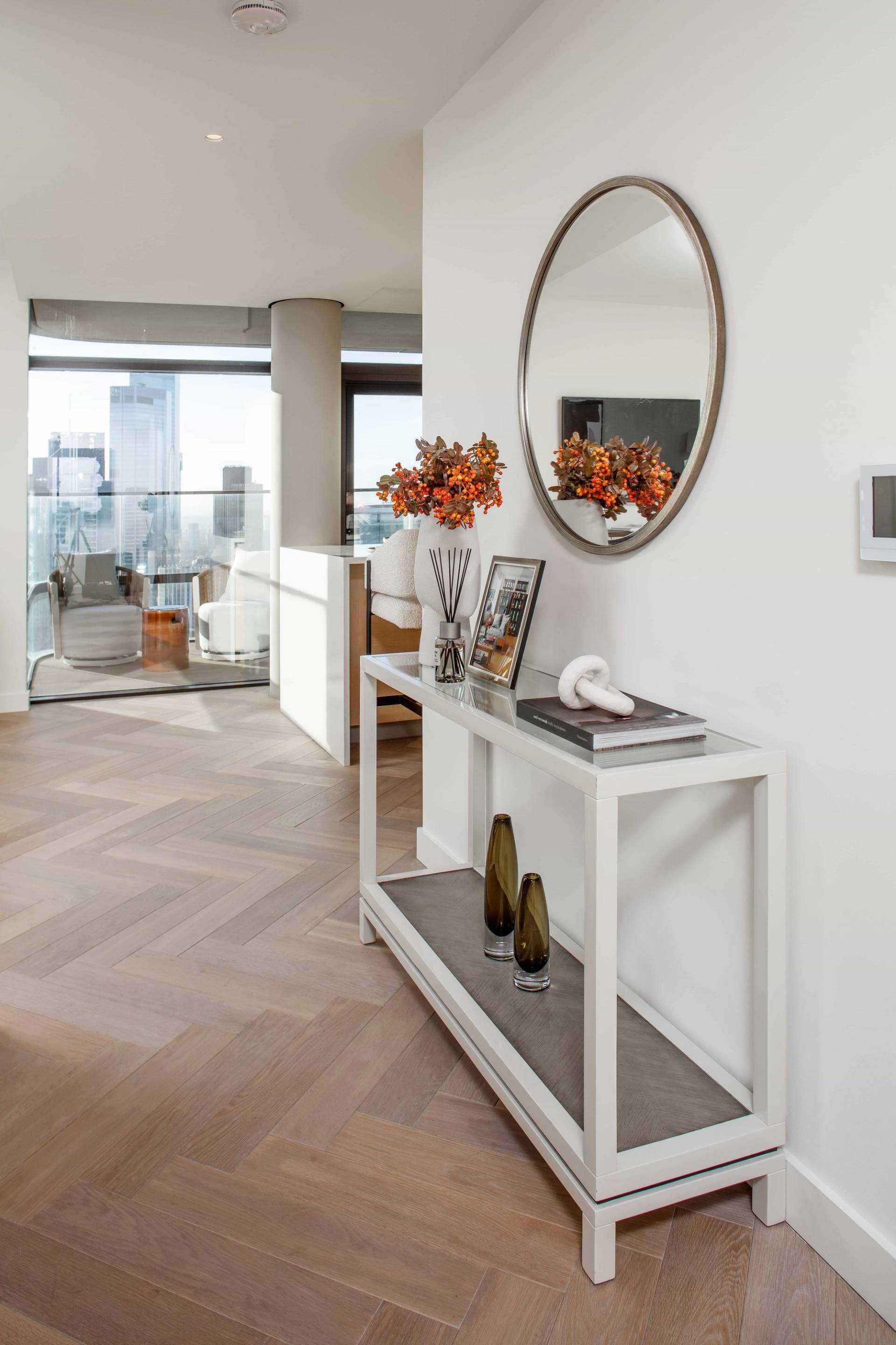 Modern penthouse entry hallway featuring a white console table, round mirror, and herringbone wood floors, ideal for establishing film scenes, Love Locations.