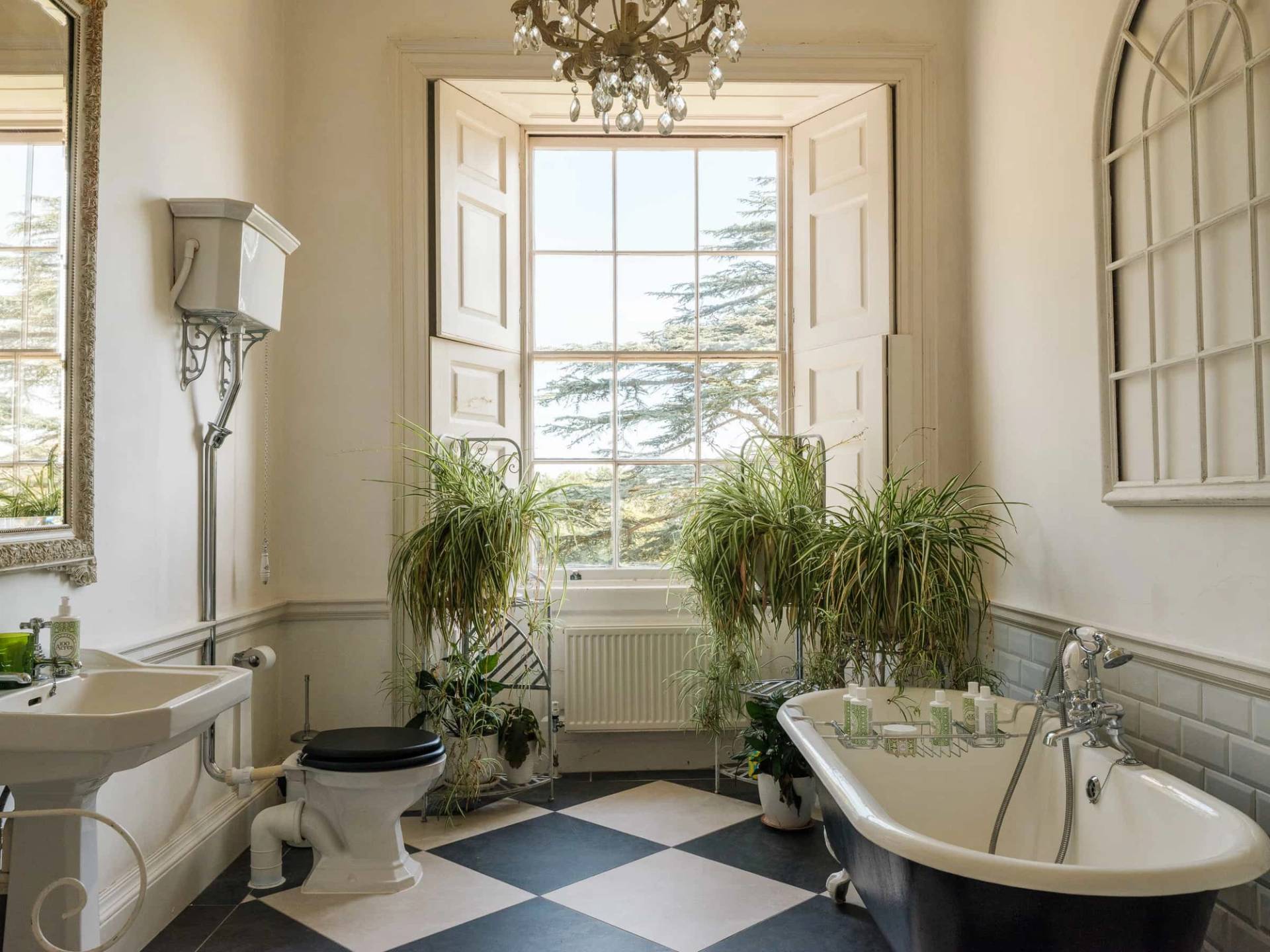 Traditional mansion bathroom featuring a roll-top bathtub, checkerboard floor tiles, and potted houseplants, Love Locations RG42.