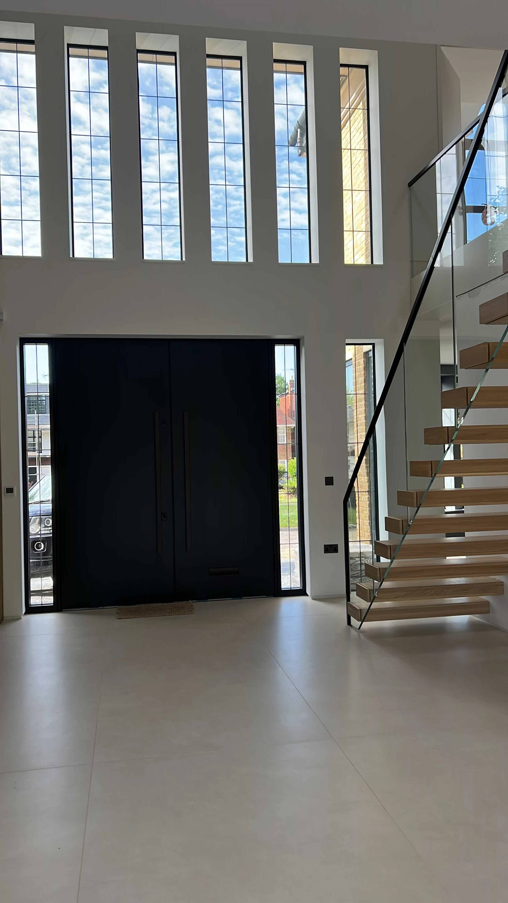 Spacious entrance foyer featuring a dramatic black front door and open timber staircase with glass railings, Love Locations.