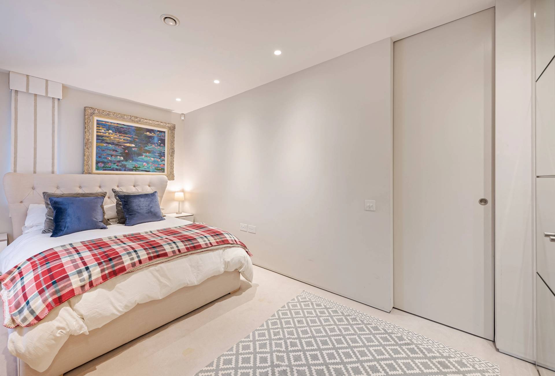 Minimalist bedroom featuring built-in wardrobes, neutral carpet, and red plaid throw blanket, Love Locations KT2.