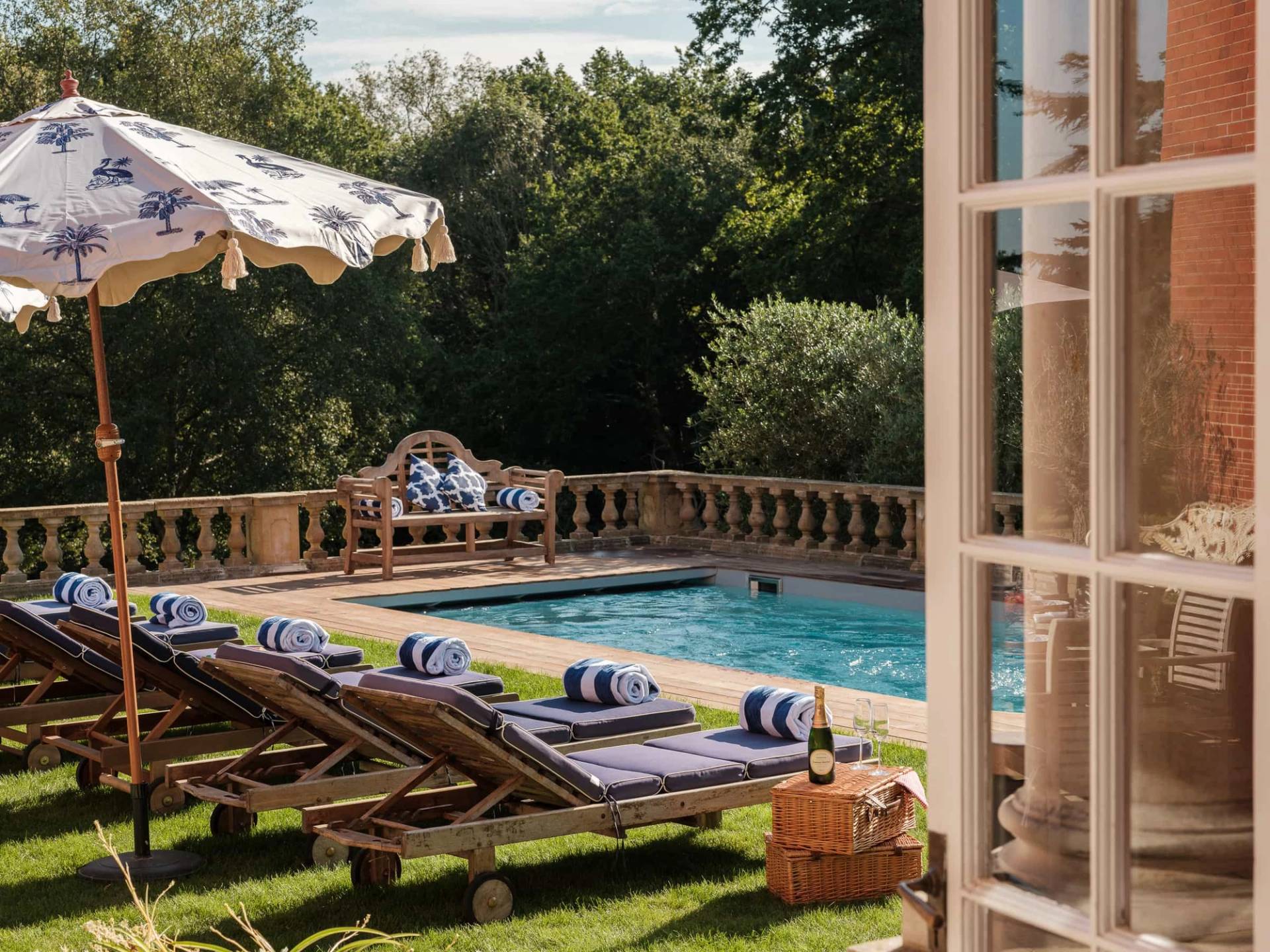 Outdoor swimming pool set on a paved stone terrace with wooden sun loungers and striped parasols, Love Locations RG42.