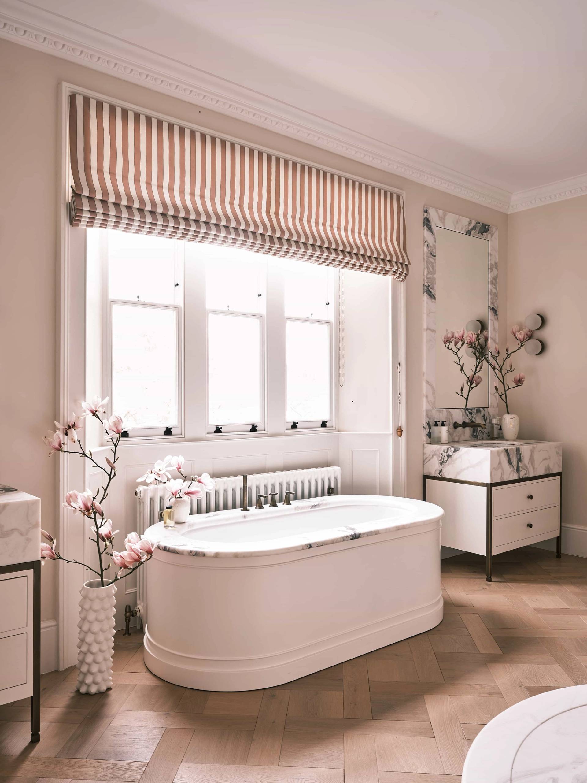 Luxury freestanding soaking tub set before a multi-pane window with striped roman blinds and marble vanities, ideal for spa product advertising, Love Locations OX7.