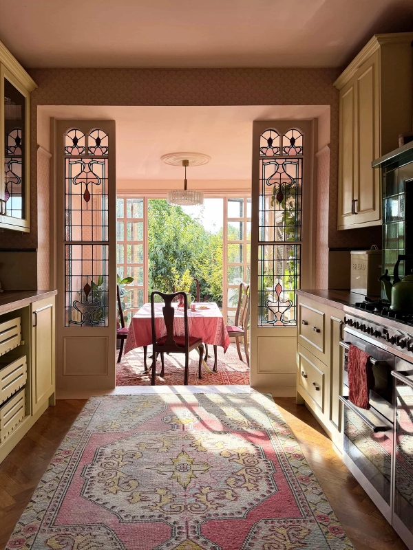 Sunlit kitchen dining space framed by original Art Deco stained glass French doors overlooking garden greenery, Love Locations N13.