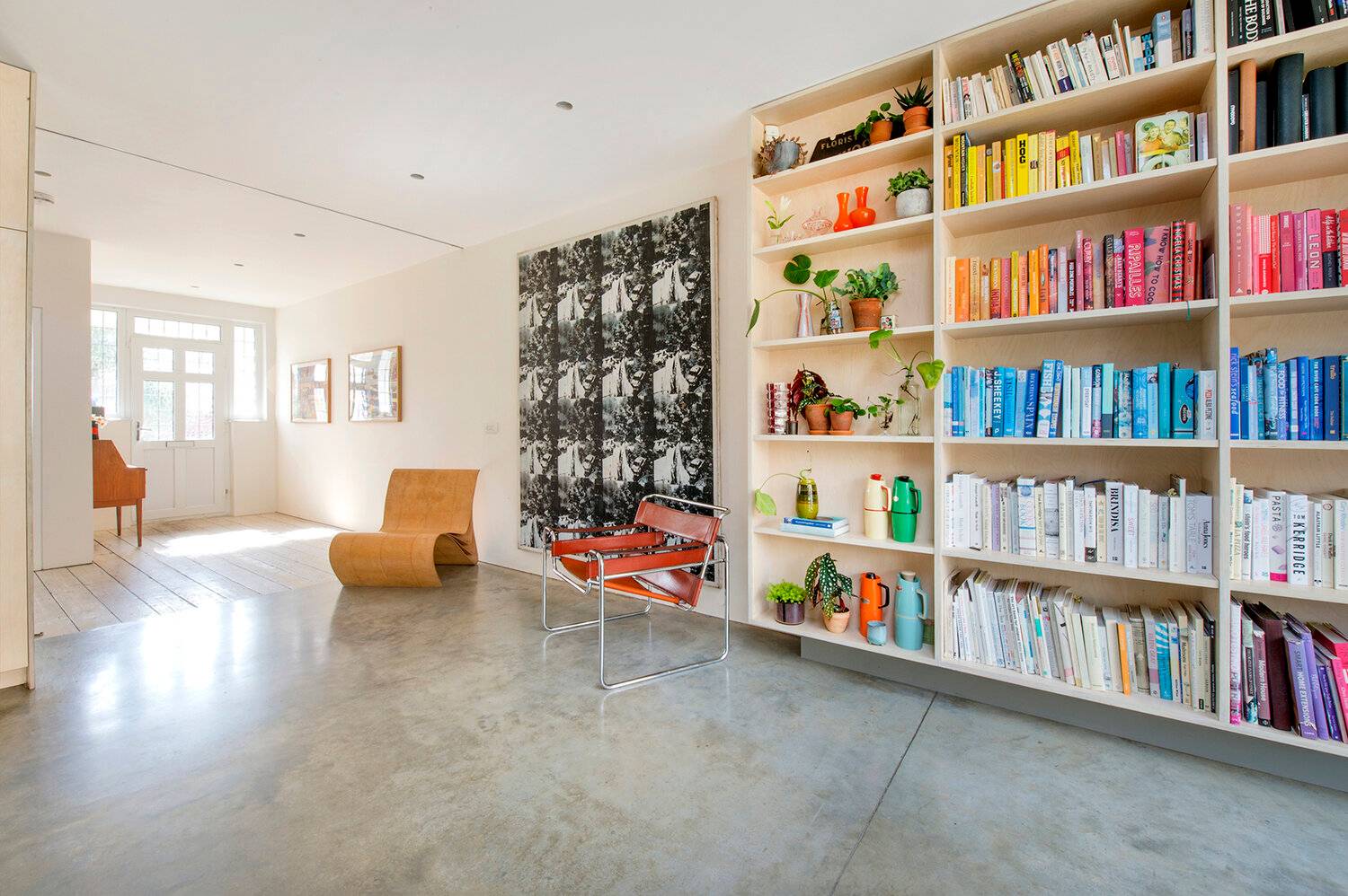Minimalist reception room featuring full-wall Birch plywood custom bookshelves, polished concrete floors, and mid-century chairs, Love Locations SE23.