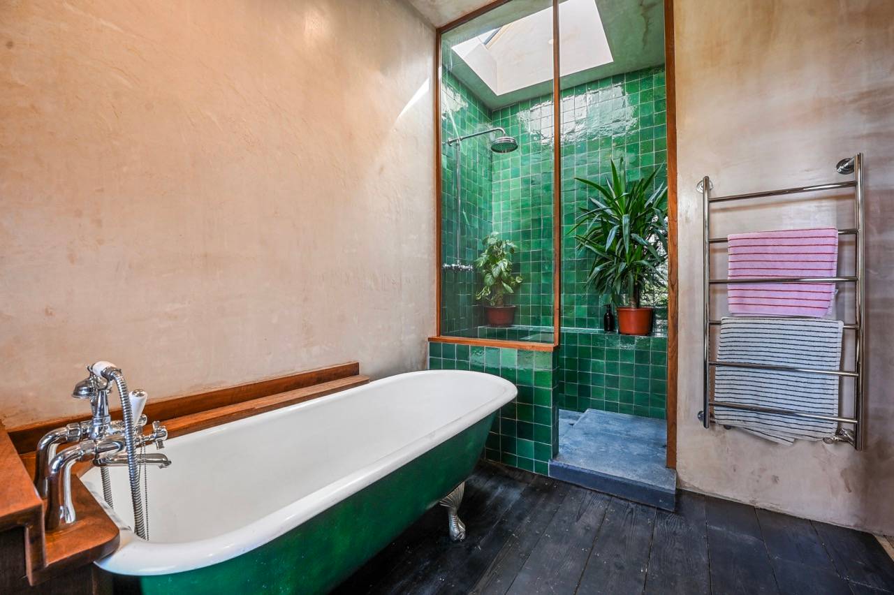 Green roll-top bath set under a skylight window with emerald green glazed tile walls, Love Locations.