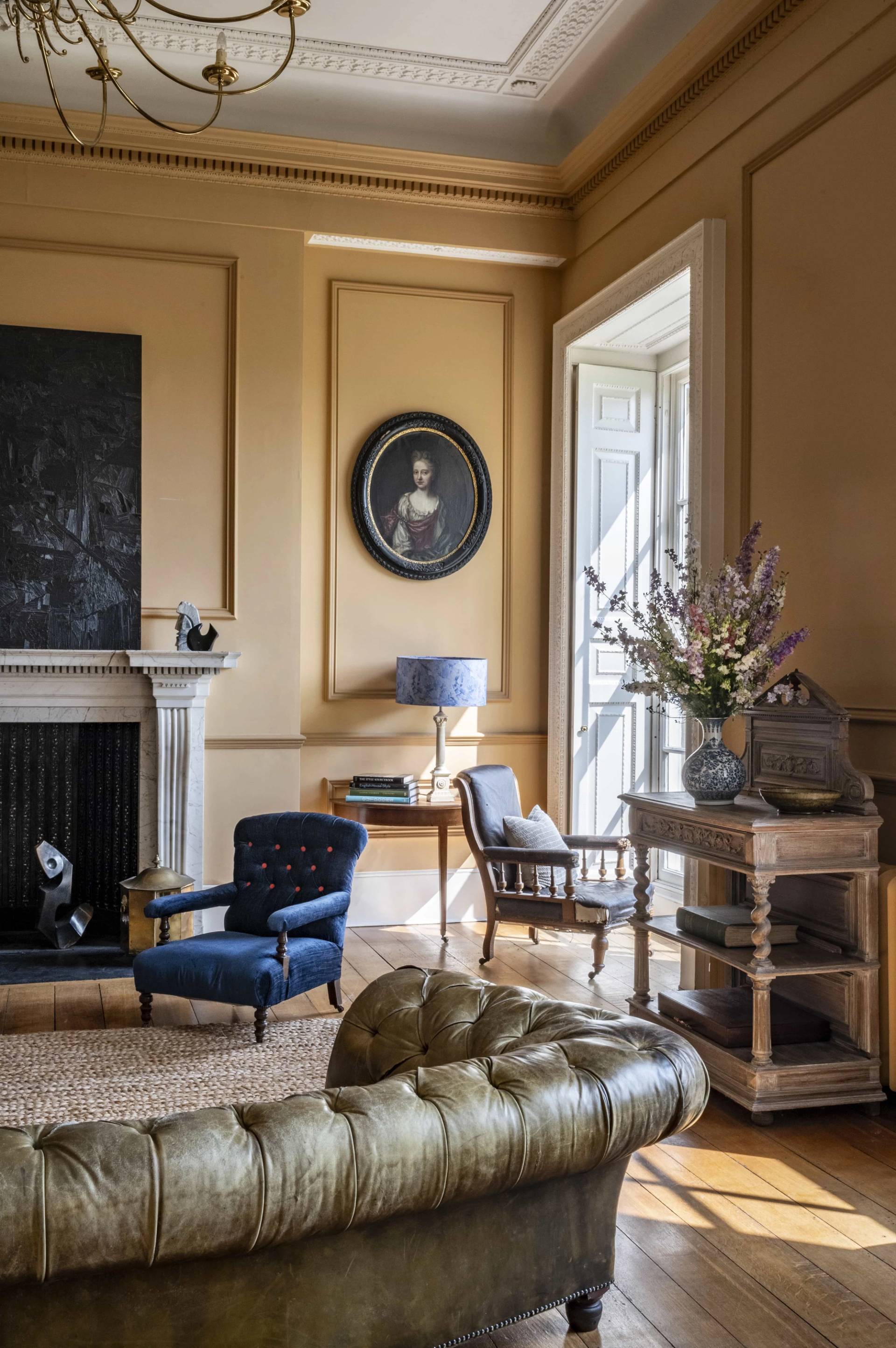 Elegantly styled ochre living room showcasing a classic Chesterfield sofa, oval wall mirror, and sash windows, perfect for heritage brand campaigns, Love Locations.