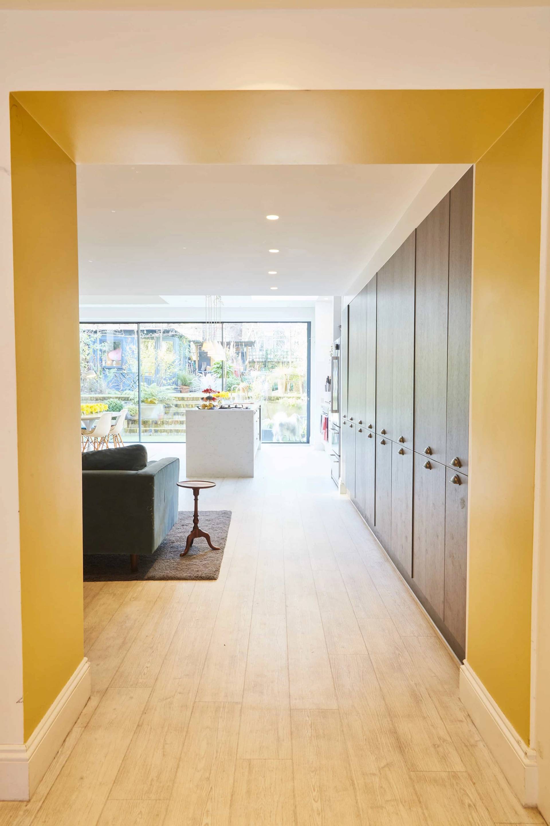 Bright hallway passage with yellow painted door frame looking into an open-plan kitchen living room in Islington, Love Locations N5.