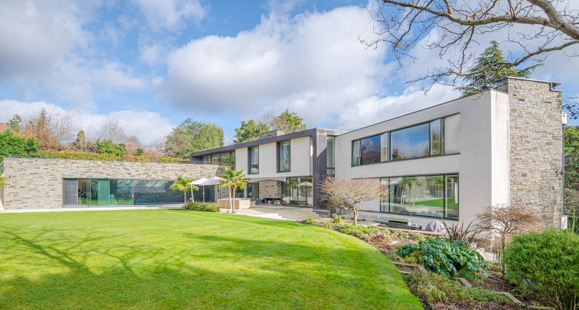 Modern architectural white mansion rear garden elevation showing floor-to-ceiling glass windows and manicured grounds, Love Locations KT2.