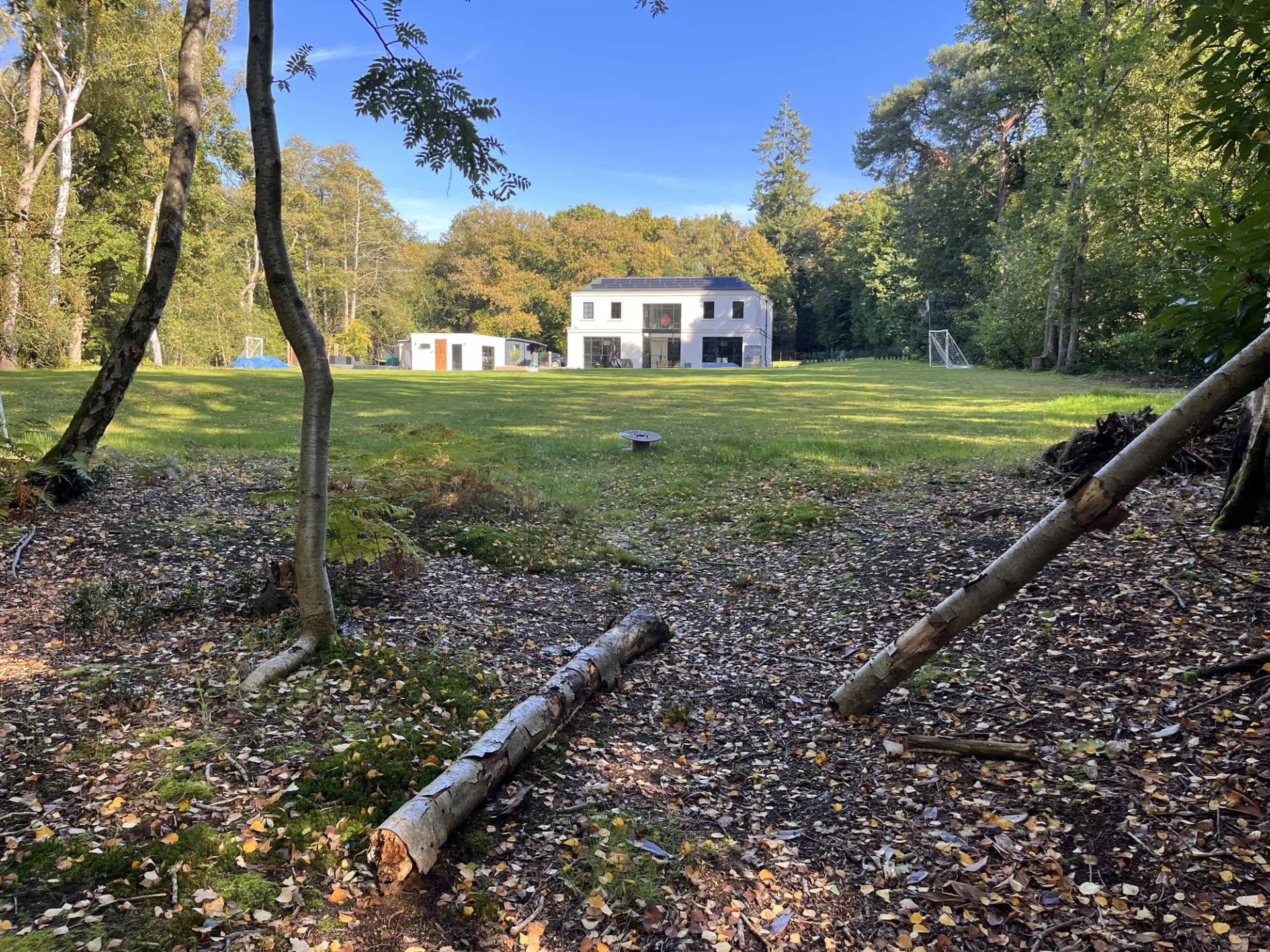 View looking through private woodland forest grounds toward a white luxury mansion shoot location, Love Locations GU3.
