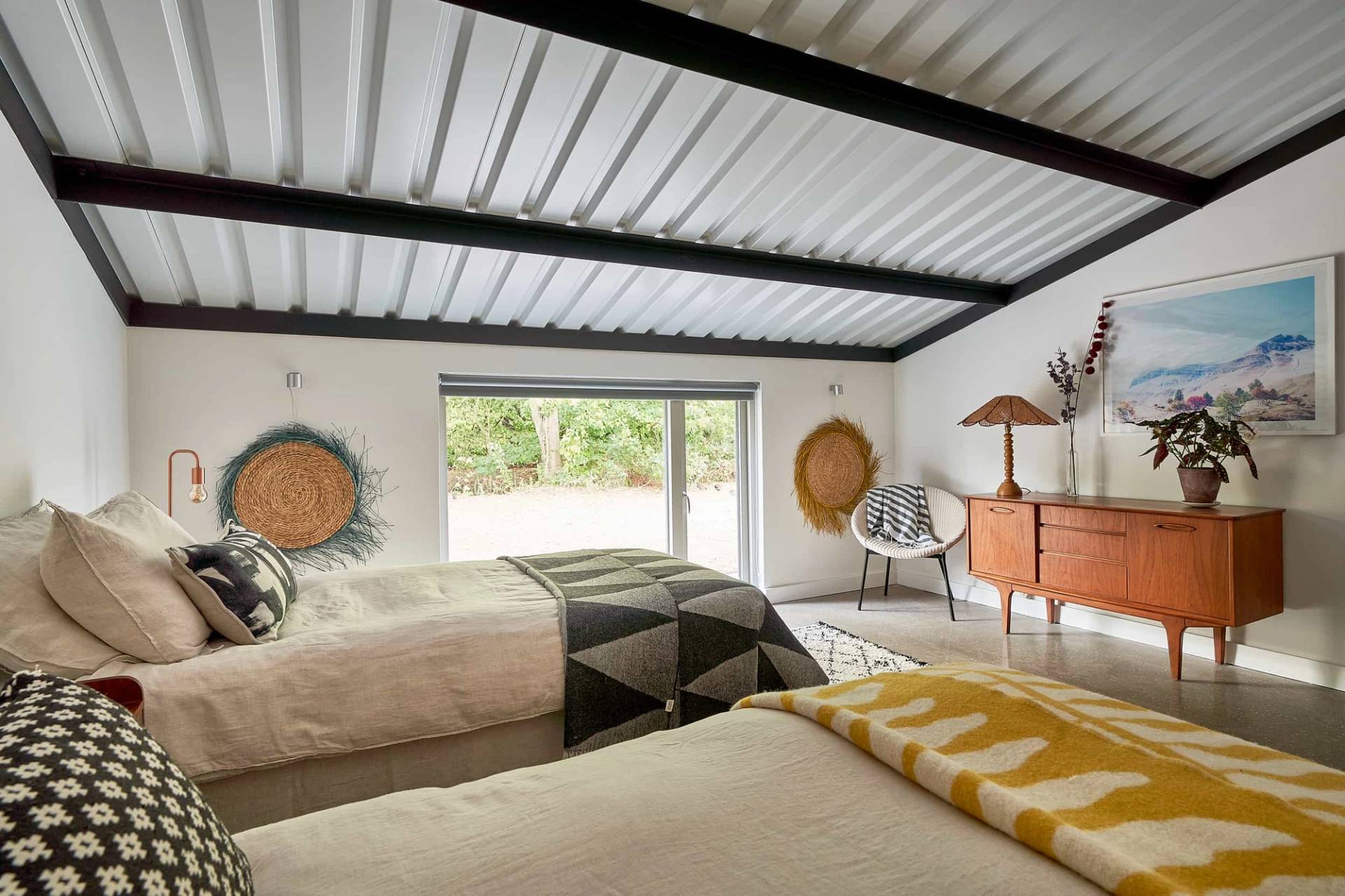 Twin guest bedroom suite with corrugated metal ceiling, geometric throws, and floor-to-ceiling glass doors, Love Locations IP30.