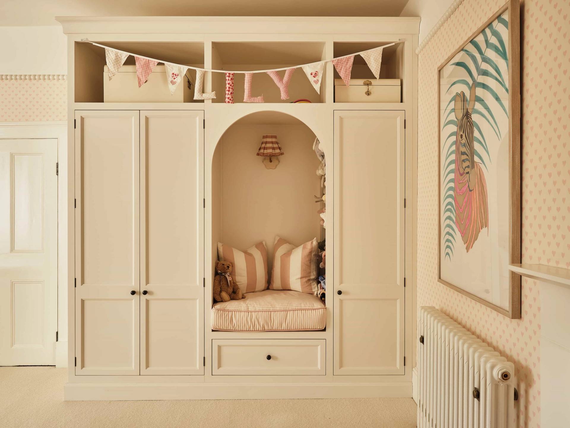 Custom built-in wardrobe storage with an arched cushioned reading nook and pink bunting, Love Locations OX7.