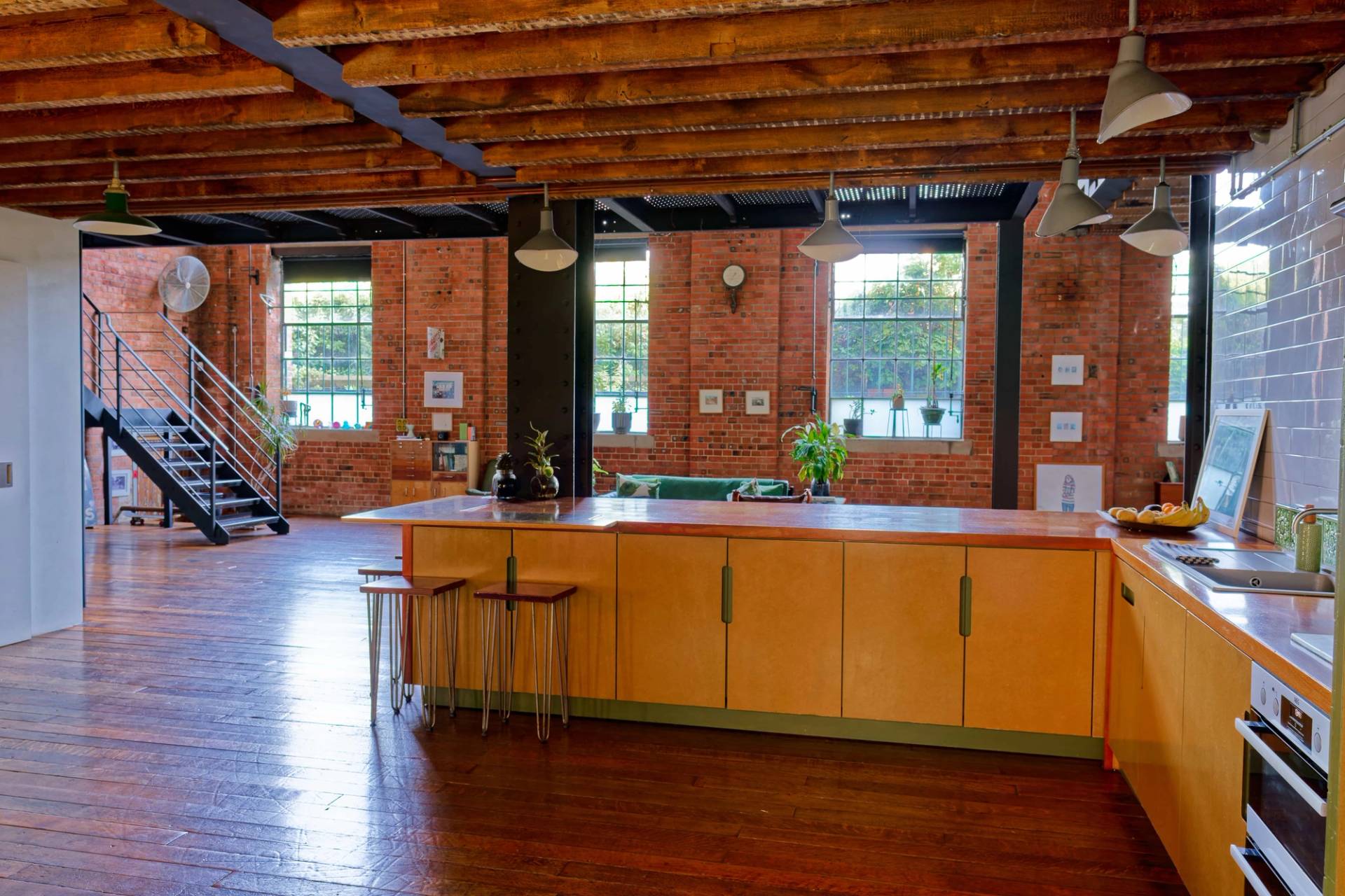 Industrial kitchen layout with yellow cabinets, wooden island, exposed brick walls, and steel structural posts in Tower Hamlets, Love Locations.