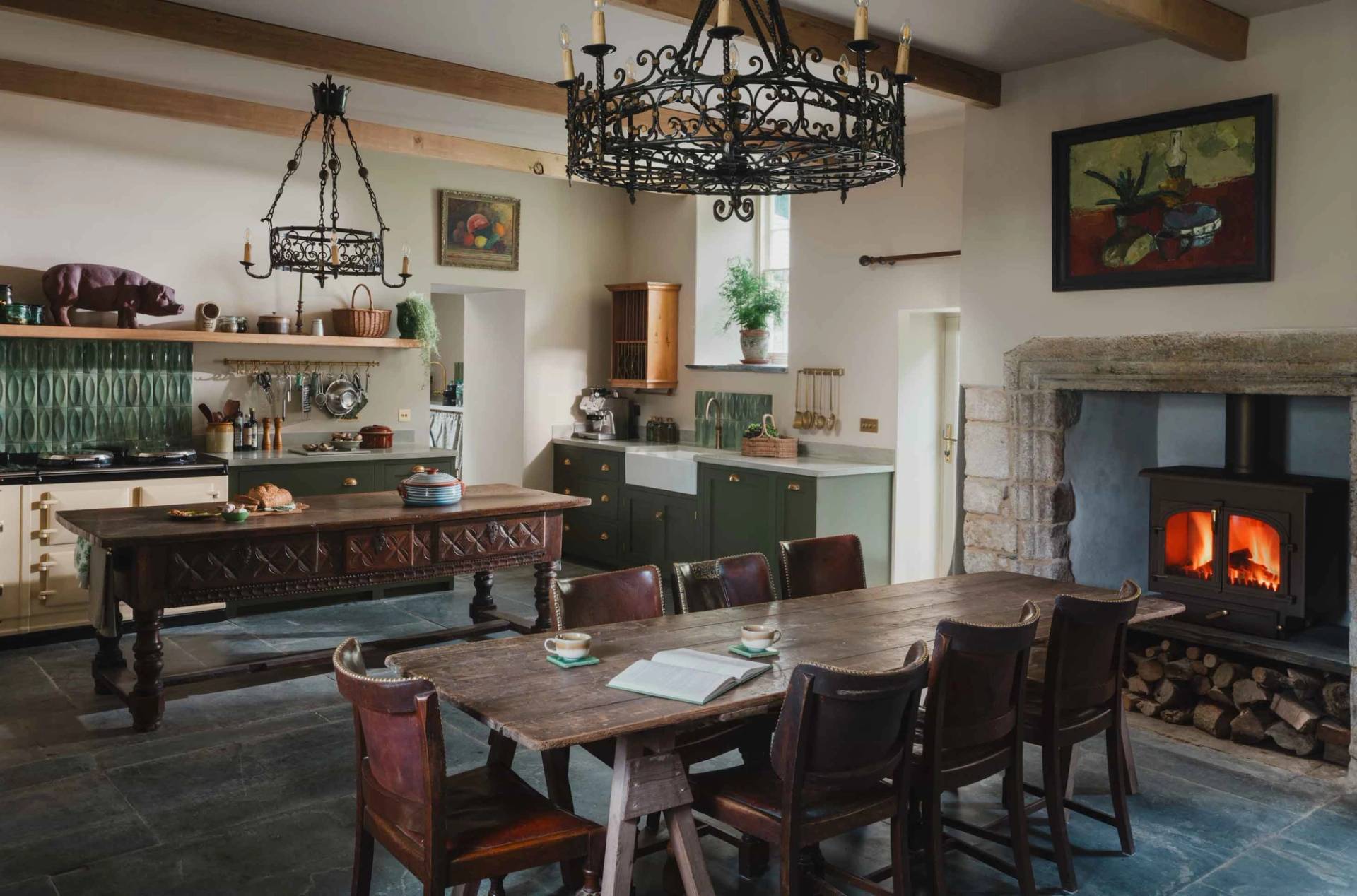 Historic country house kitchen and dining space in a Grade II-listed Cornish manor in Newquay Cornwall TR8 via Love Locations, featuring a long rustic wooden dining table, stone walls, and a wrought-iron chandelier.