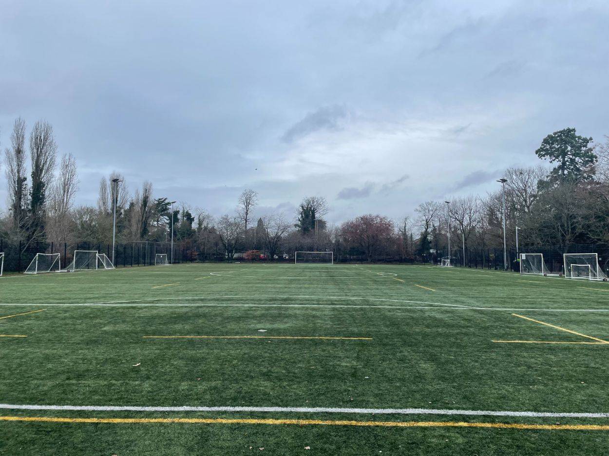 Love Locations synthetic turf location RG30: Ground-level tracking shot across an all-weather football and sports field under an overcast sky, excellent for athletic training scenes.