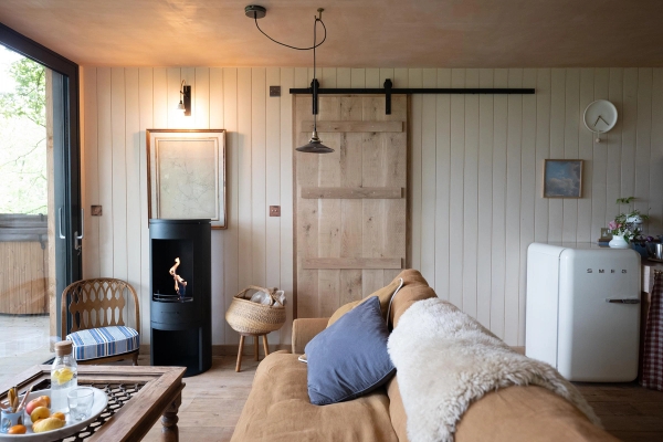 Warmly lit cabin lounge shoot space showing a modern black wood-burning stove and a sliding timber barn door, available via Love Locations HR4 8ls.