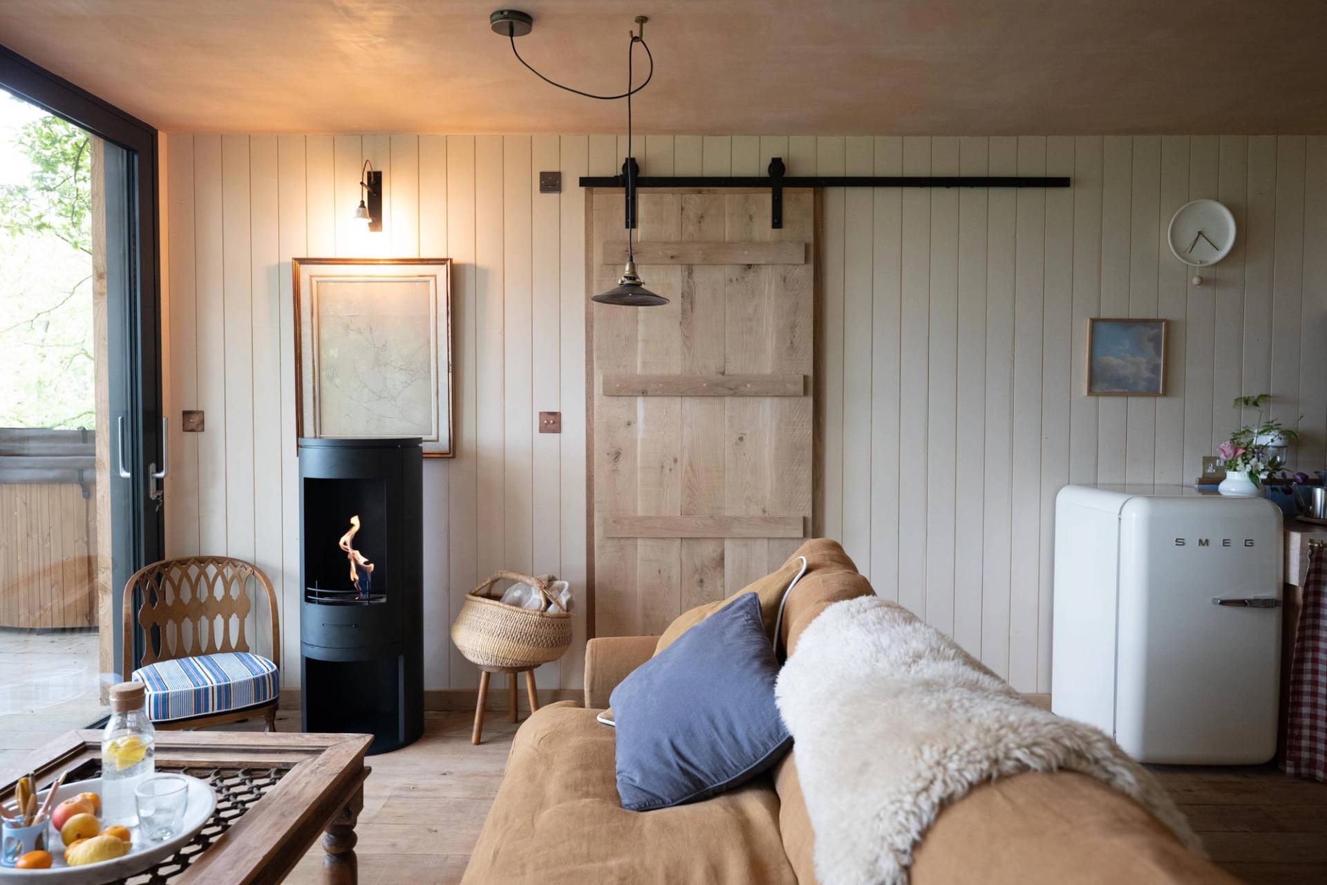 Warmly lit cabin lounge shoot space showing a modern black wood-burning stove and a sliding timber barn door, available via Love Locations HR4 8ls.