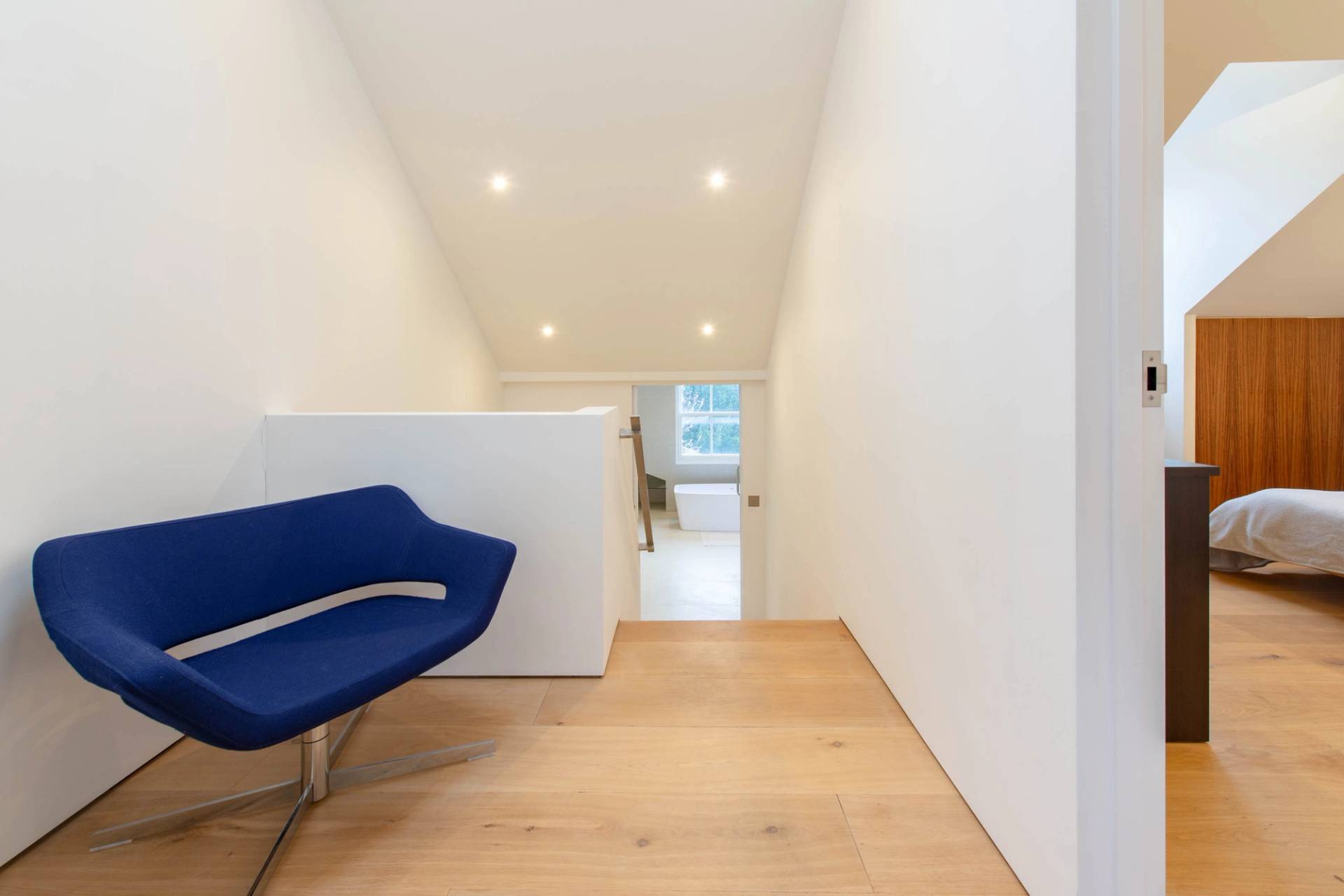 Upper hallway landing transition with a blue accent chair, white walls, and natural wood floorboards, Love Locations SW6.
