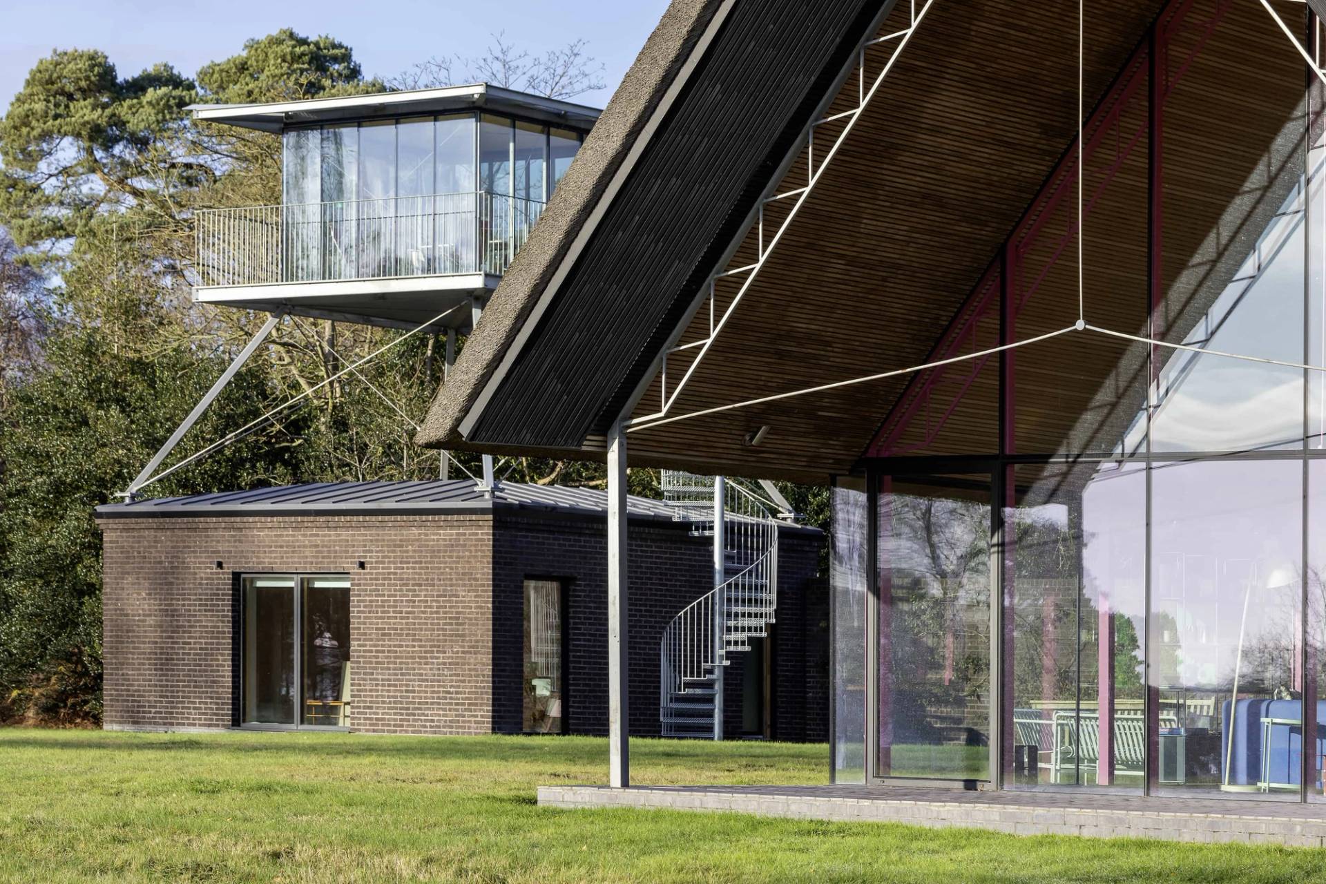 Architectural view showing the connection between a modern thatched longhouse and a raised glass lookout tower, Love Locations IP17.