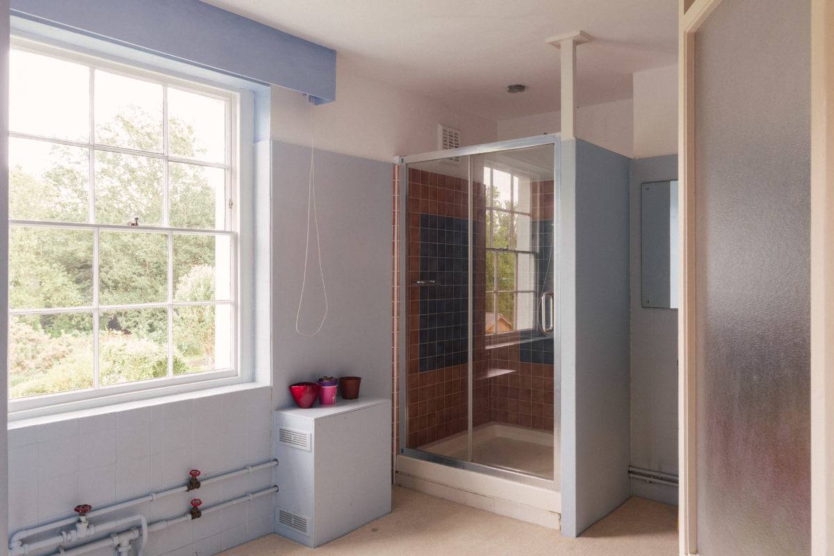 Light blue tiled bathroom suite featuring a glass shower enclosure and sash window views, Love Locations SE15.