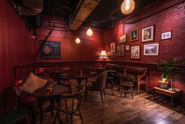 Alternative view of an atmospheric crimson-hued restaurant dining area with authentic antique furniture and exposed industrial piping, suitable for television drama scenes, Love Locations SW16.