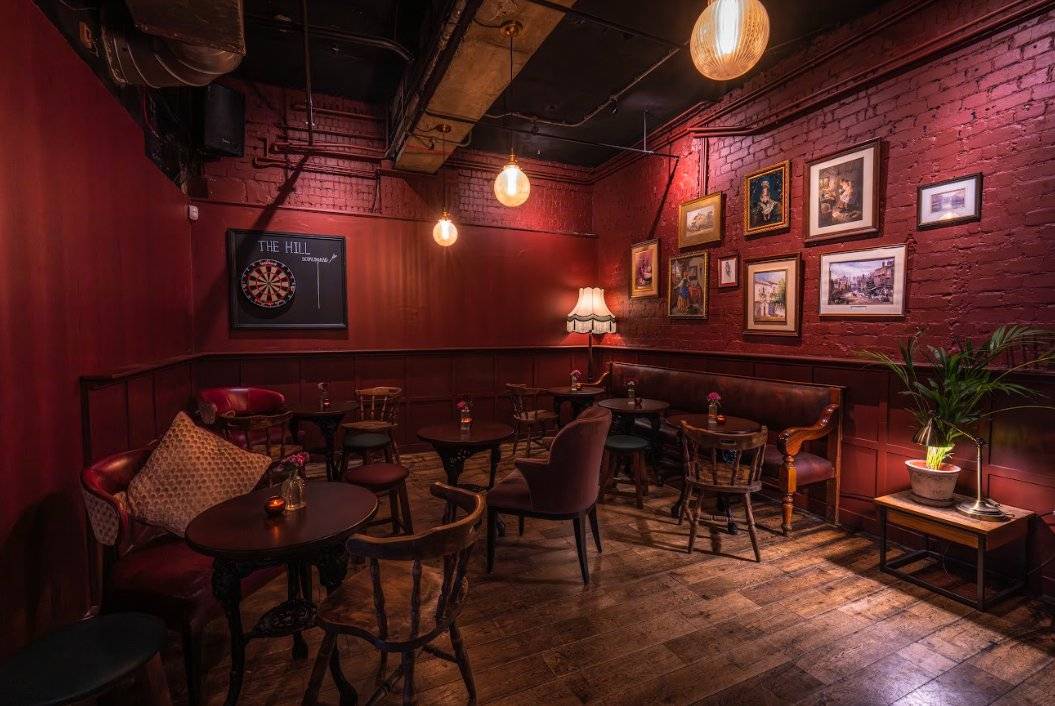Alternative view of an atmospheric crimson-hued restaurant dining area with authentic antique furniture and exposed industrial piping, suitable for television drama scenes, Love Locations SW16.