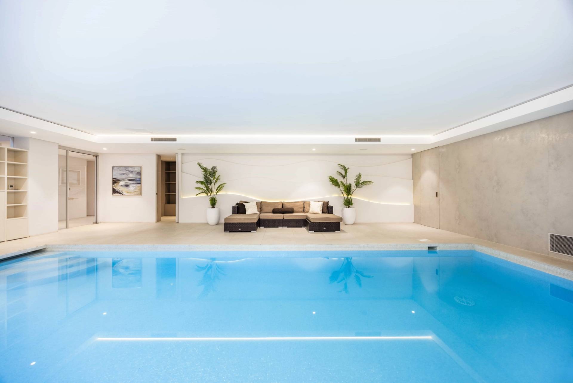 Wide-angle perspective of an indoor lap pool with smooth white surround and ambient ceiling lighting, Love Locations WD7.