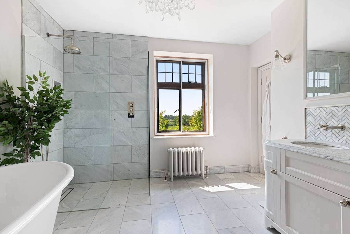 Modern bathroom with grey stone shower tiles, leaded window, and white porcelain fixtures, Love Locations RH13.