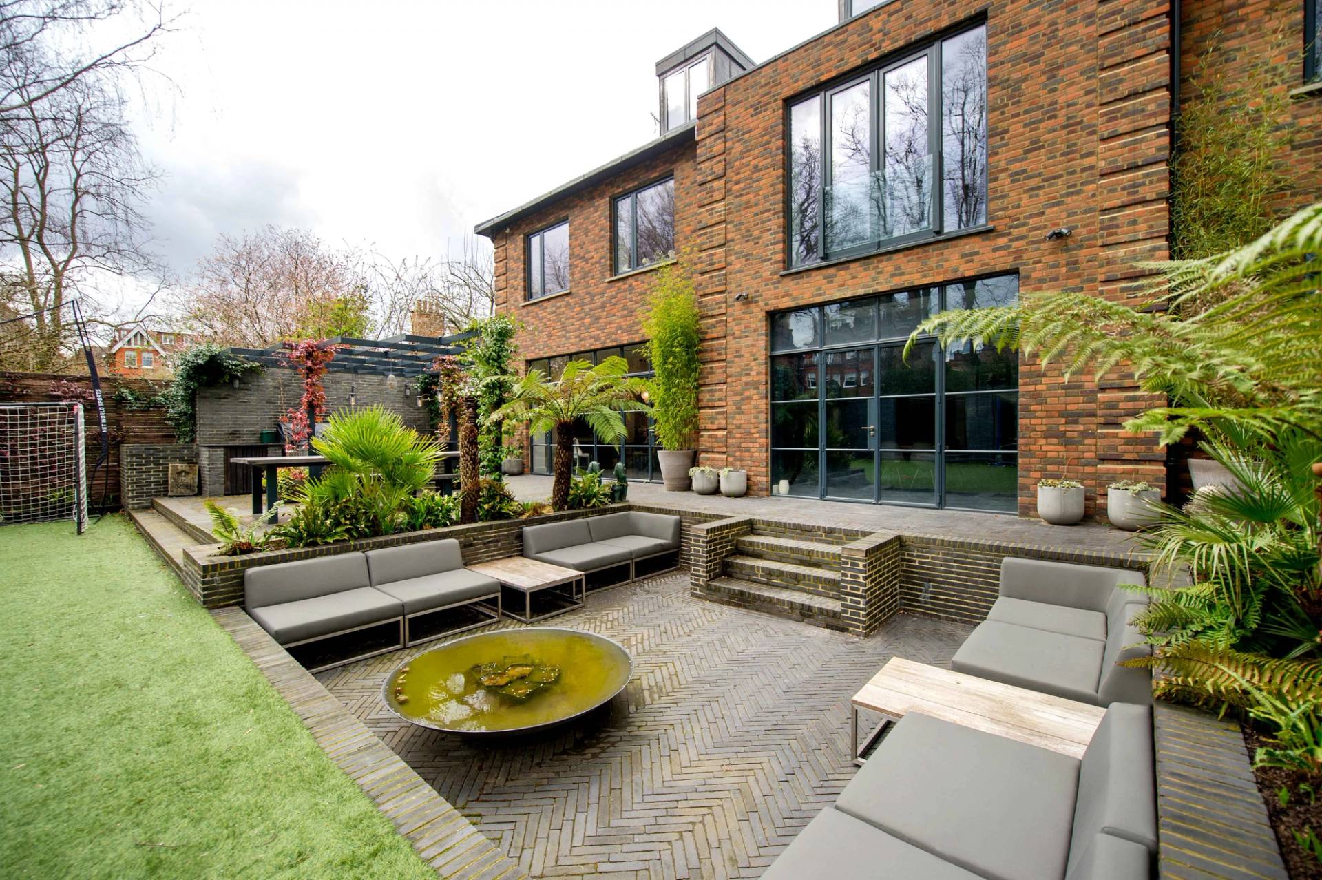 Designer outdoor sunken lounge seating area set within a stone patio overlooking a green lawn in North London, Love Locations NW3.