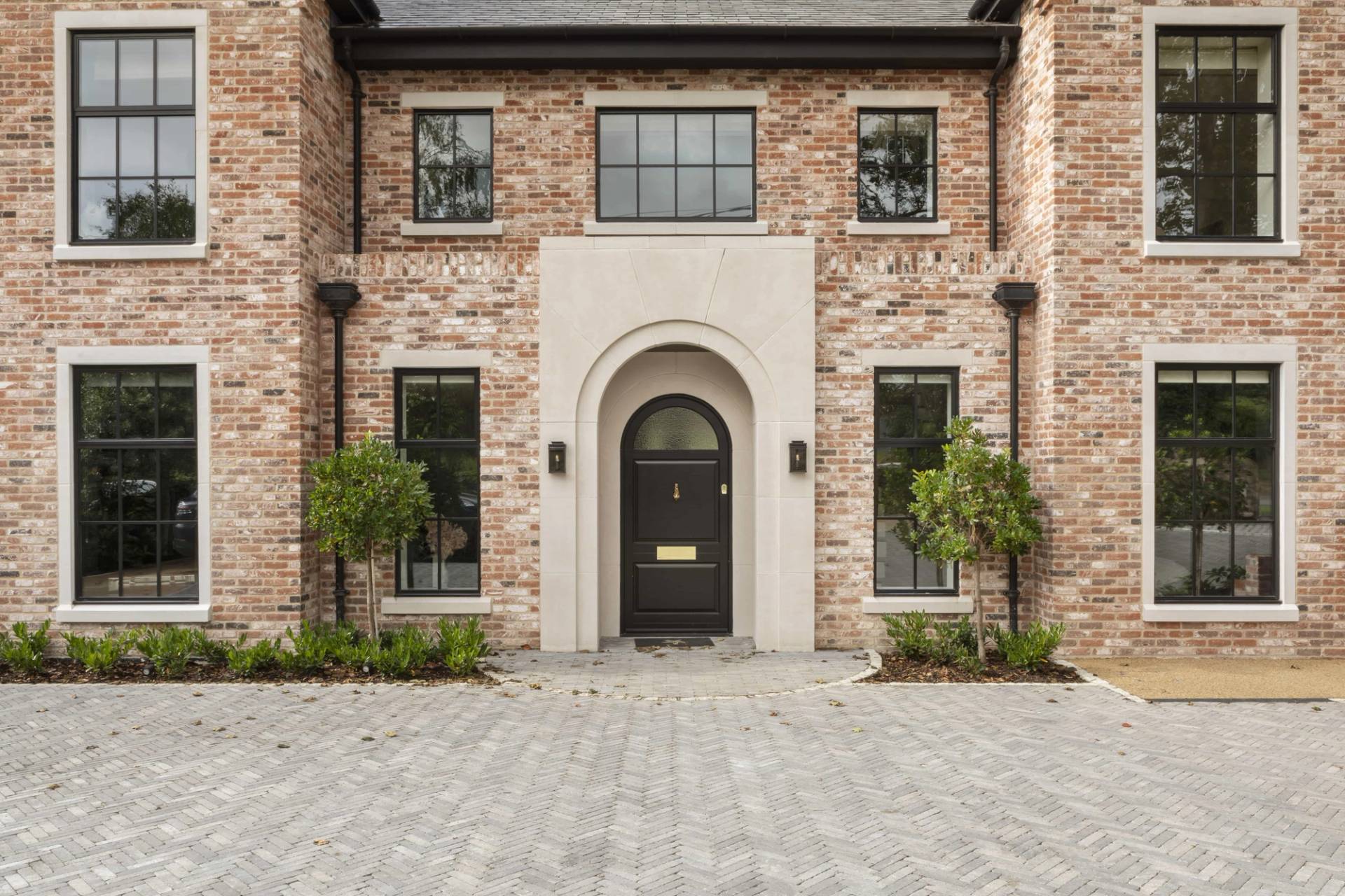 Grand red brick mansion front entrance featuring an arched portico, black arched front door, and paved driveway, Love Locations HP18.