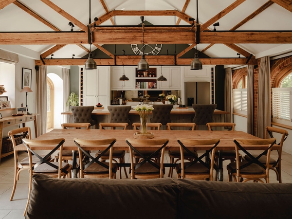 Symmetrical interior view of a vaulted barn dining space with wooden cross-back chairs and exposed timber beams in Nuffield, RG9, perfect for food editorial media filming, Love Locations.