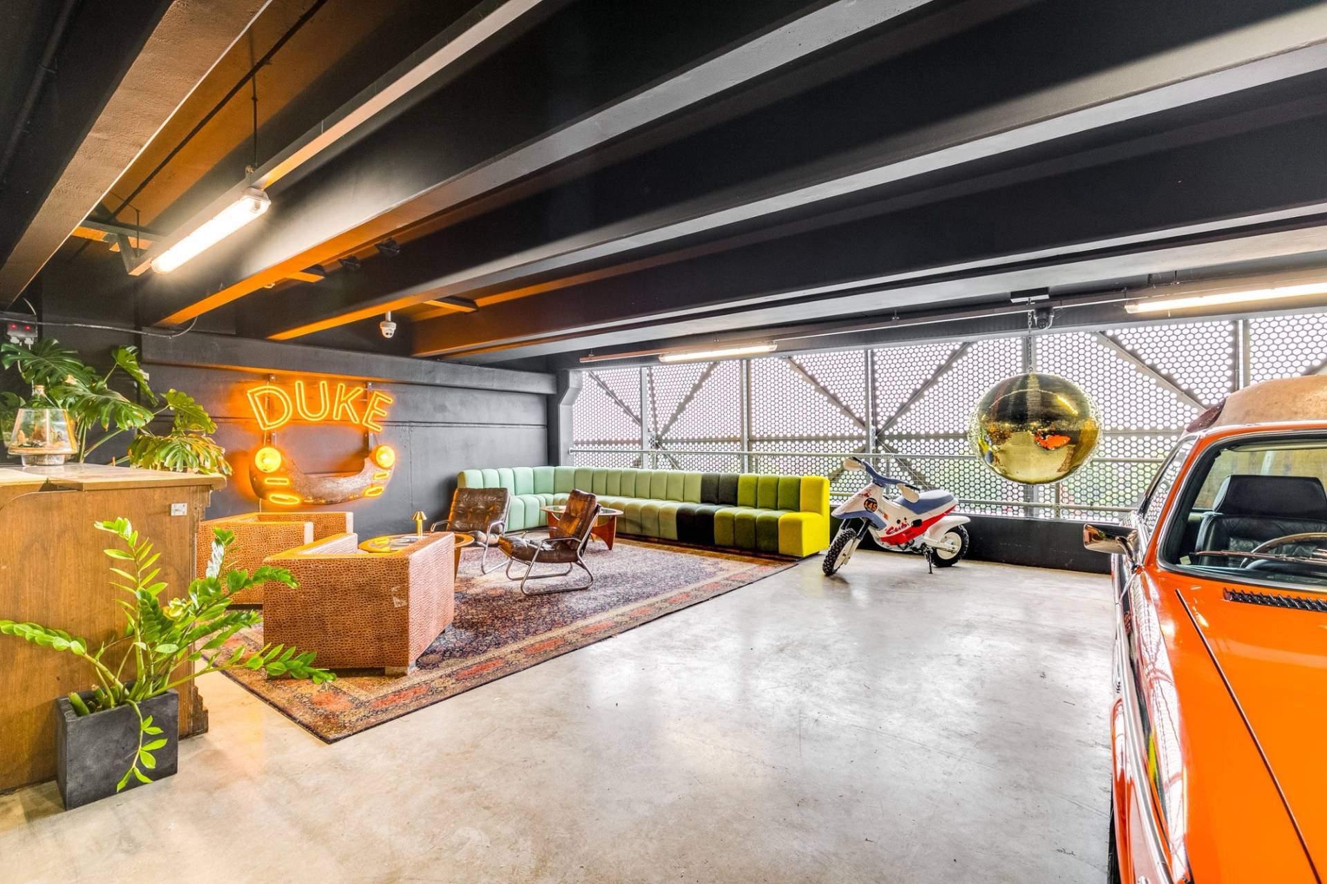 Sprawling industrial car showroom production venue in Brentford TW8 by Love Locations, featuring polished concrete flooring, a gold disco ball, and retro seating layout.
