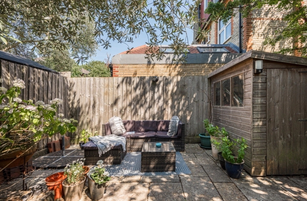 Cosy garden terrace terrace corner featuring a dark rattan outdoor corner sofa set and a timber garden storage shed, Love Locations.