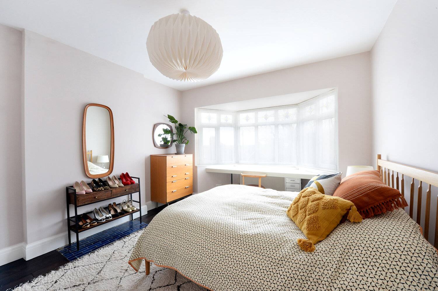 Serene bedroom setup with a low wooden bed frame, textured throw pillows, mid-century dresser, and round wall mirror, Love Locations SE23.