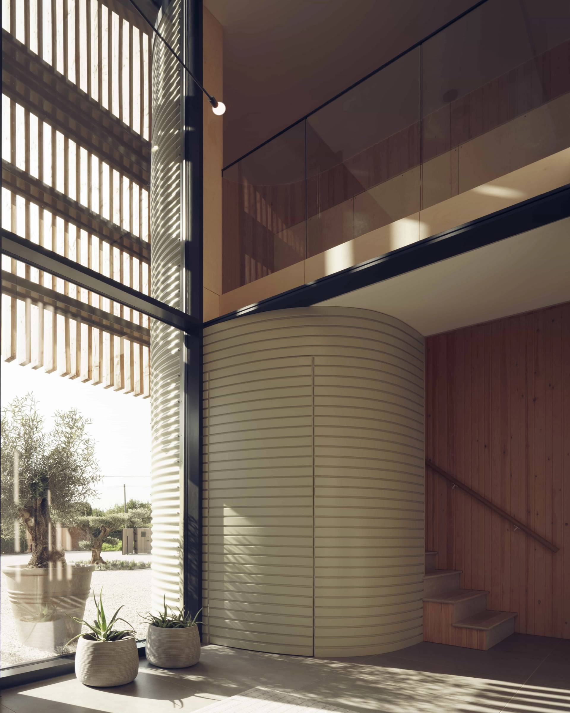 Bespoke curved fluted timber entrance wall set under a double-height glass atrium and mezzanine walkway, Love Locations NR9.