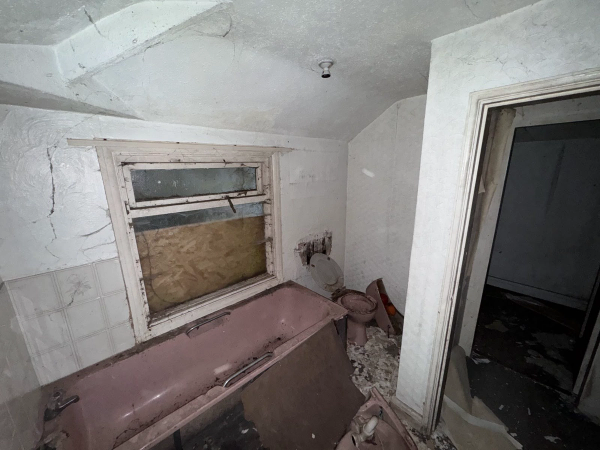 Spooky abandoned bathroom featuring a vintage dusty pink bathtub surrounded by collapsed ceiling plaster, listed on Love Locations.