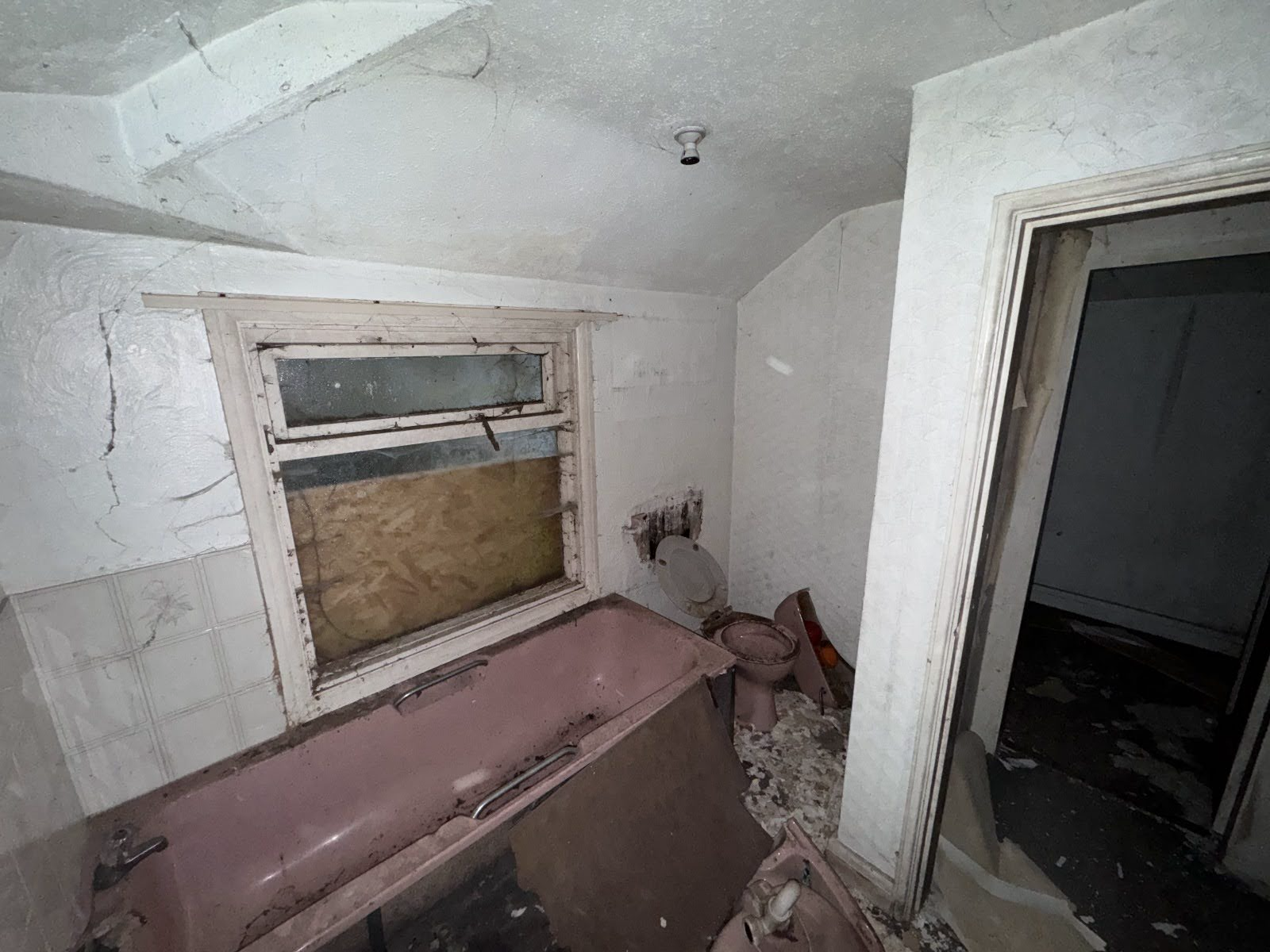 Spooky abandoned bathroom featuring a vintage dusty pink bathtub surrounded by collapsed ceiling plaster, listed on Love Locations.