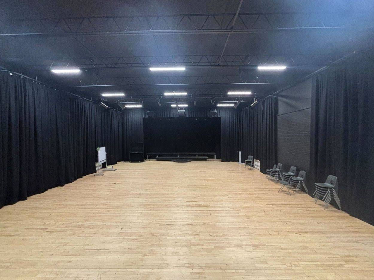 Black box drama studio photo location featuring black drapes, light wood flooring, and theatrical overhead lighting in Kent by Love Locations.