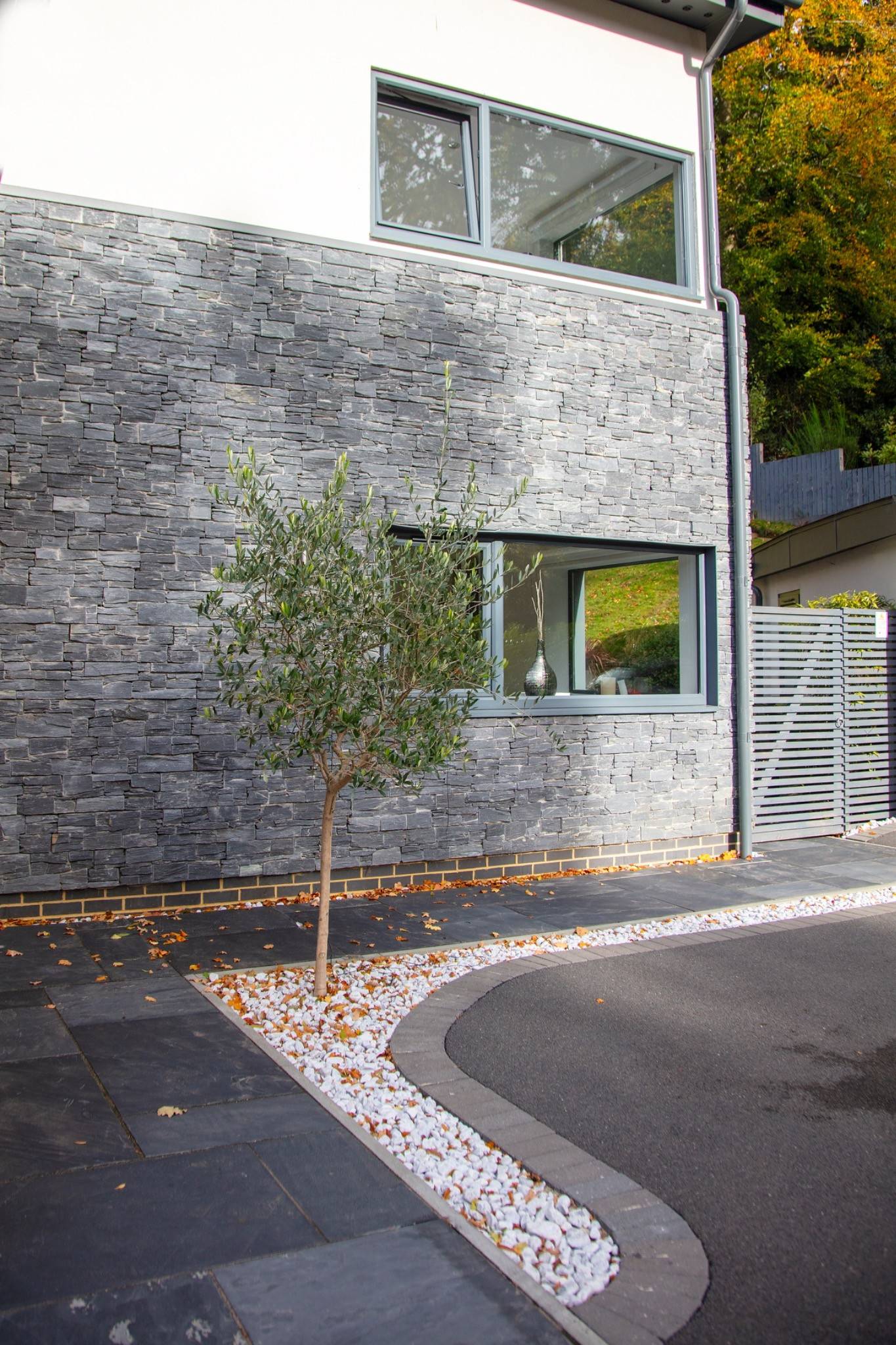 Detailed view of a premium split-face grey stone wall facade framing an olive tree container plant, curated by Love Locations.