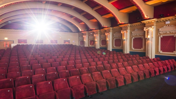 Angled perspective showing the atmospheric warm lighting, curved decorative ceiling arches, and rows of red theater seats at The Ritzy Screen 1 via Love Locations.