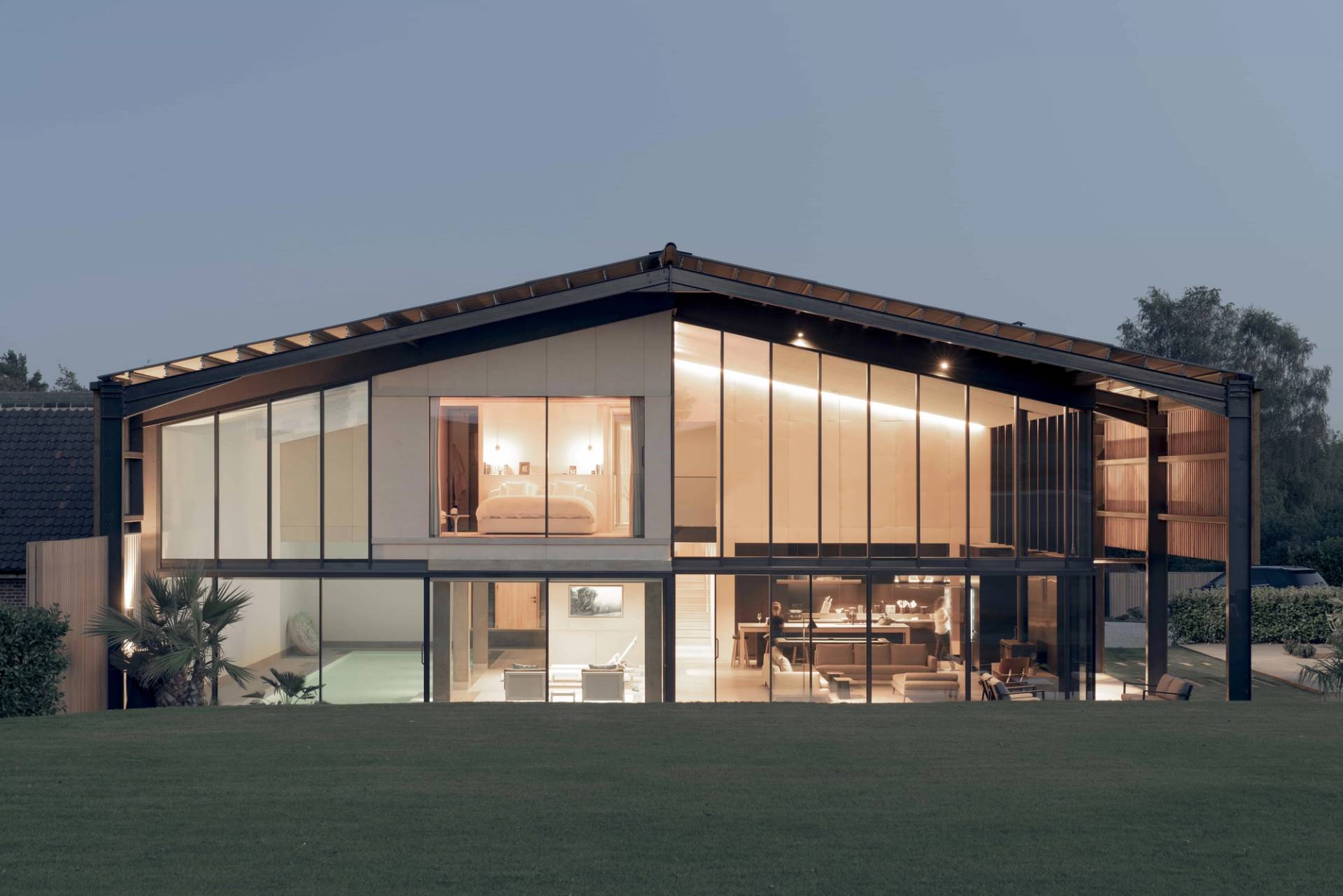 Dramatic night view of an illuminated modern barn conversion featuring full glass facades and warm internal lighting, Love Locations NR9.