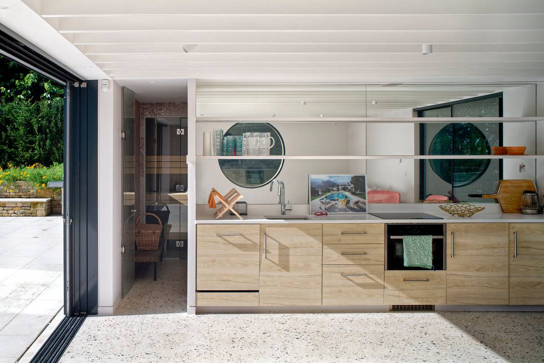 Modern pool house kitchen featuring plywood cabinets, terrazzo counter, and glass doors, Love Locations OX7.