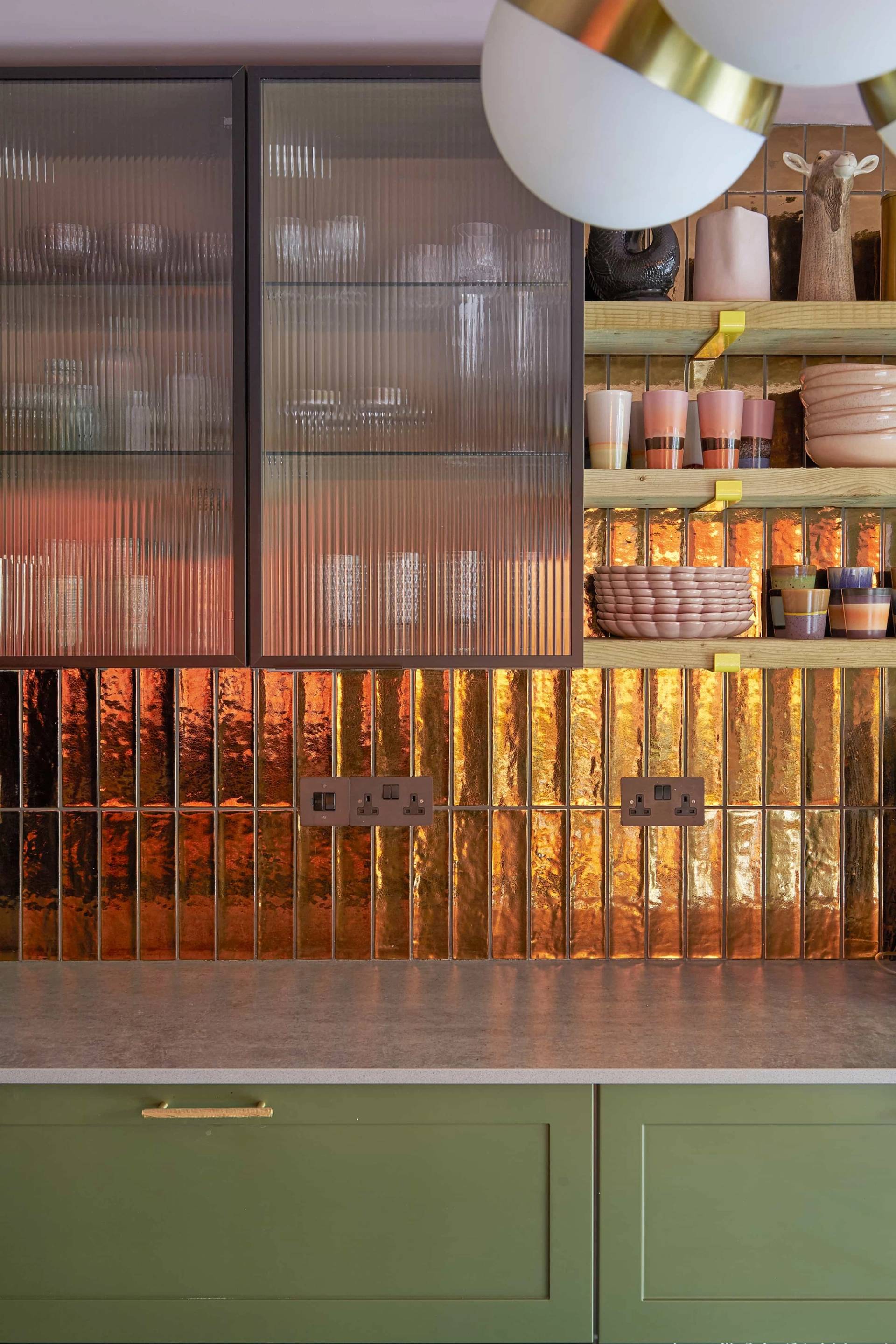 Fluted metallic copper splashback detail set under reeded glass upper cabinet doors in an olive green kitchen, Love Locations Catford.