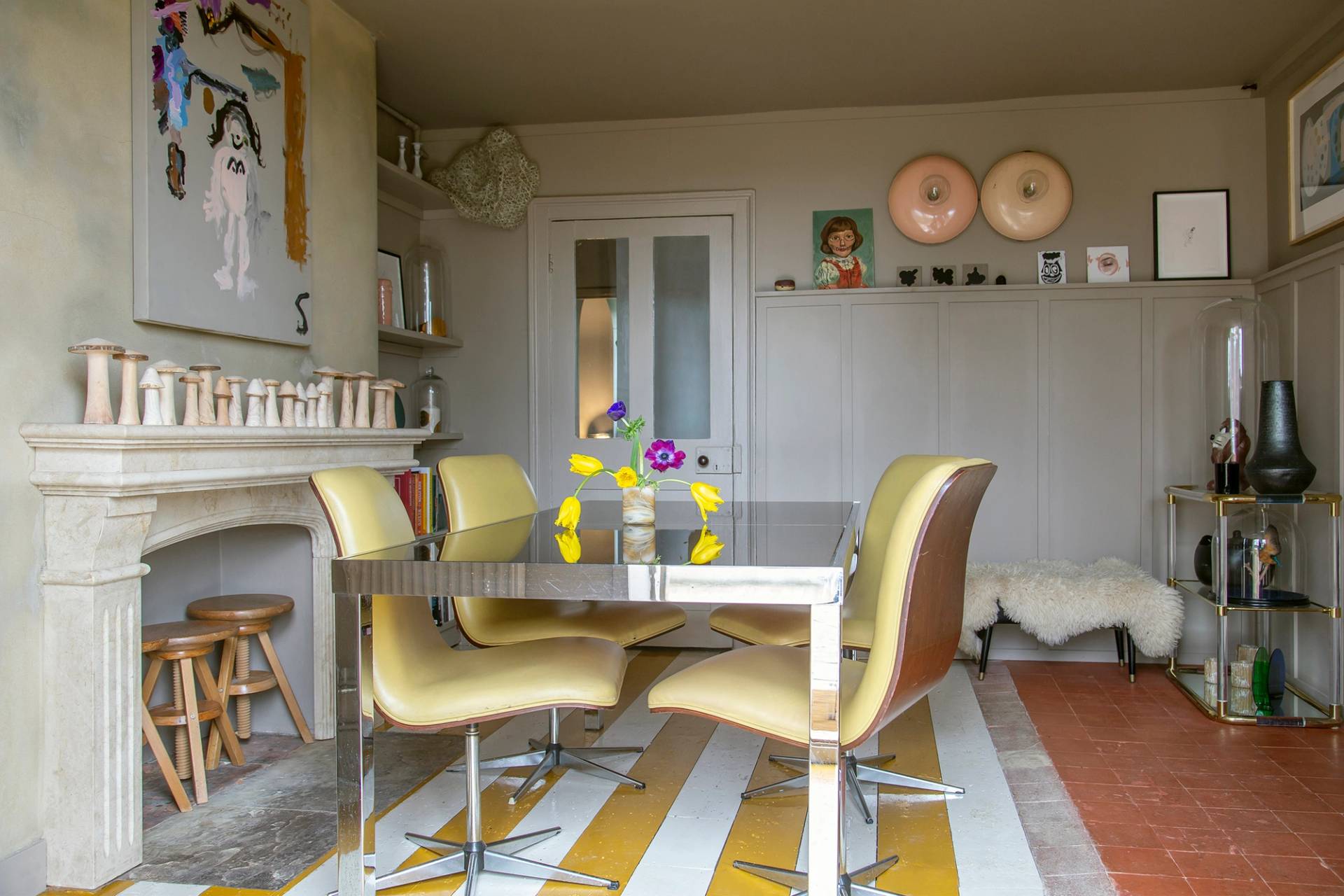 Dining space set with a chrome glass dining table, mustard chairs, yellow-striped rug, and art prints, Love Locations ME13.