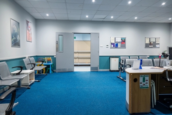 Hospital waiting room location with blue carpets, reception counter, and double entrance doors, Love Locations UB4.